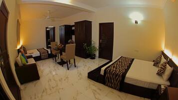 A hotel room with a bed, a sofa, a dining area, and a ceiling fan.