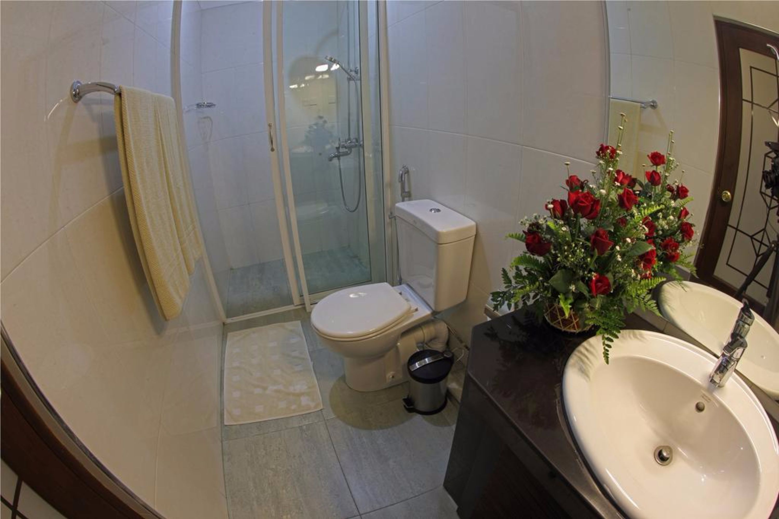 A bathroom with a toilet, shower, sink, and a decorative flower arrangement.