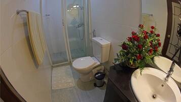 A bathroom with a toilet, shower, sink, and a decorative flower arrangement.