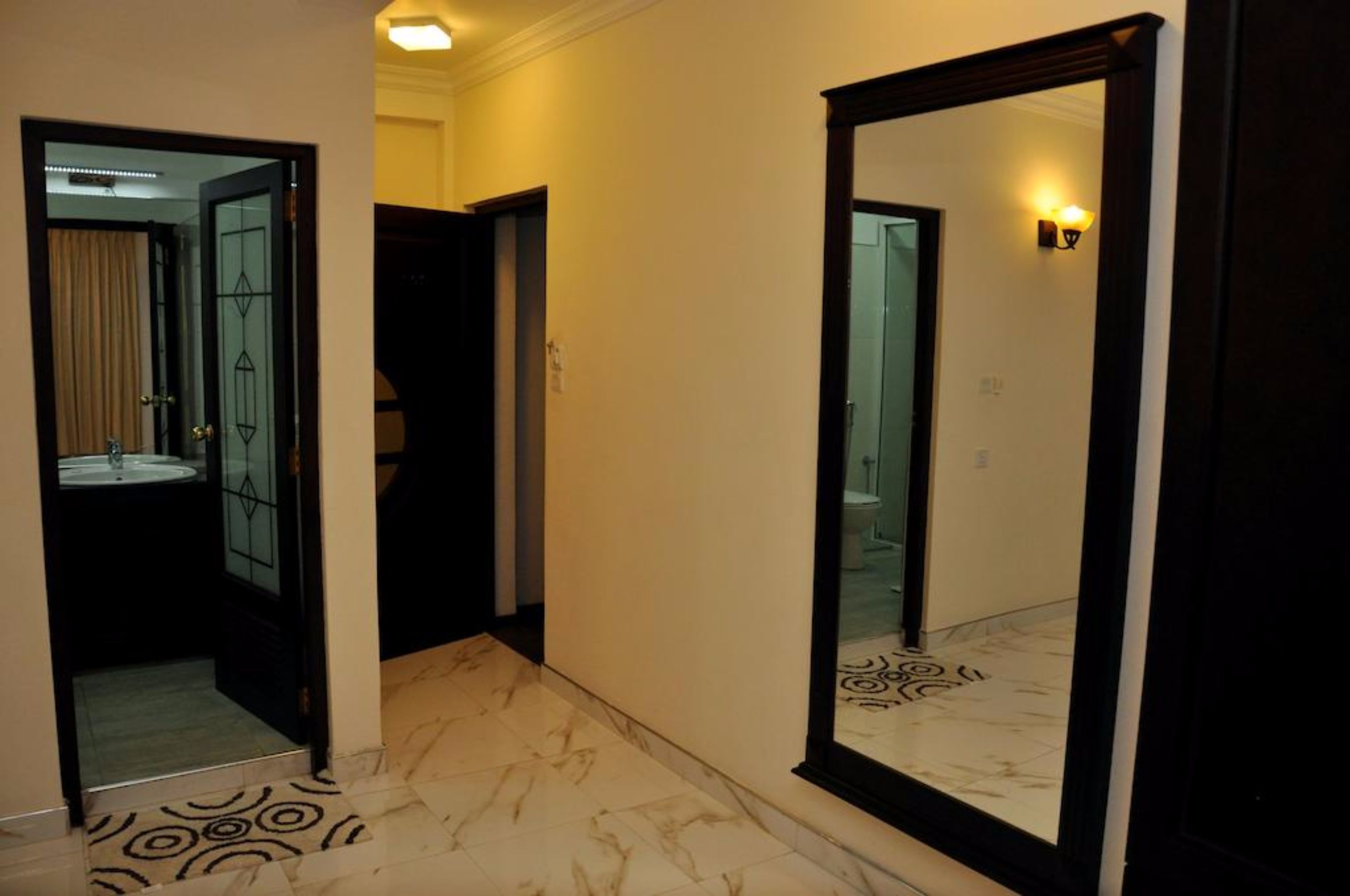 A hallway with a marble floor, a large mirror, and a door leading to a bathroom.