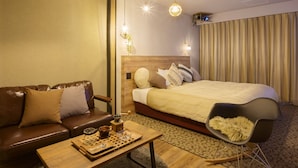 Una habitación de hotel con cabecera de madera, una cama grande, un sofá de cuero marrón, una mesita con bandeja y una silla negra.