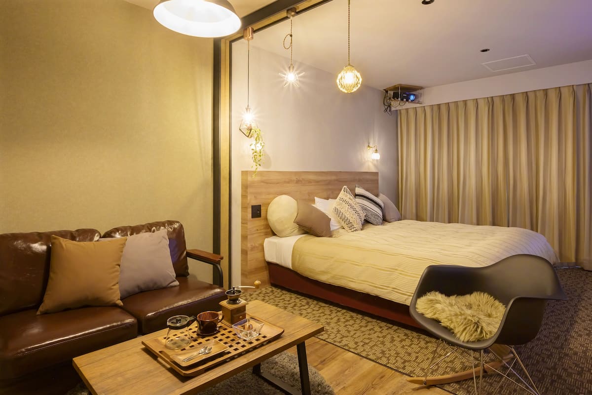 Hotellihuone, jossa on puinen sängynpääty, suuri sänky, ruskea nahkasohva, pieni pöytä tarjottimella ja musta tuoli.