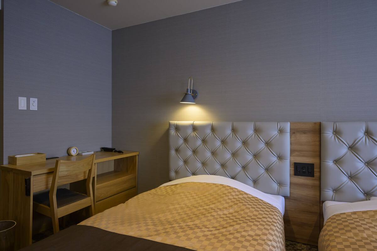 Hotellihuoneessa on sänky, työpöytä ja tuoli. Seinällä on lamppu.