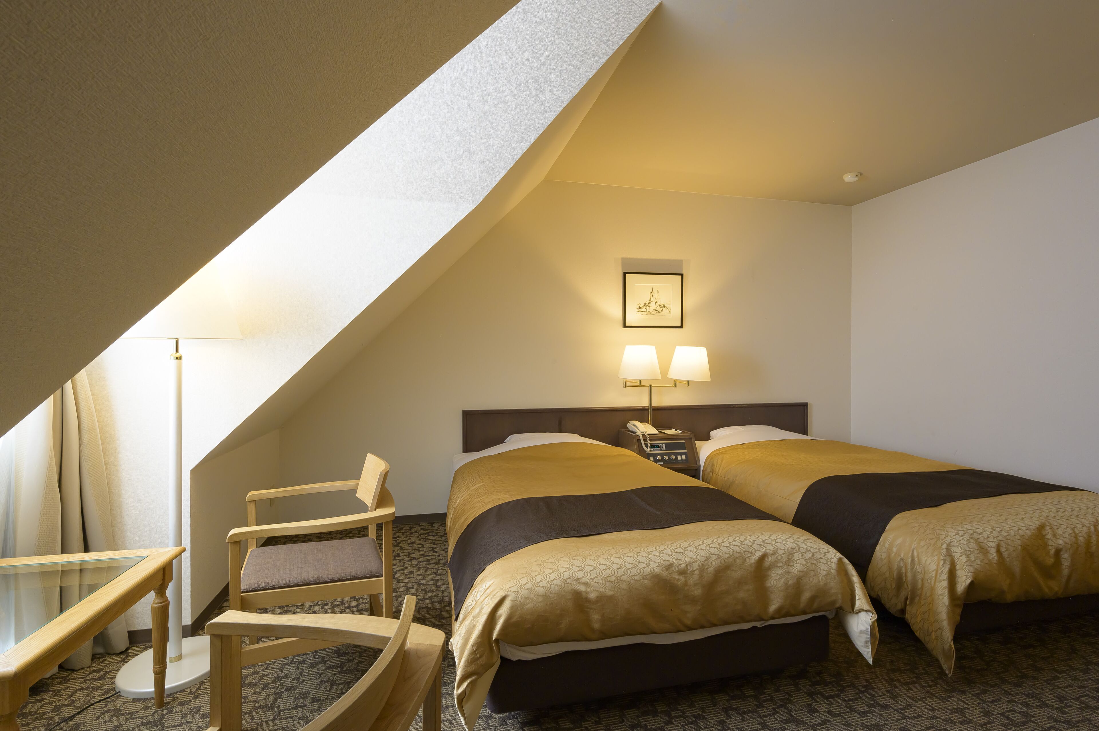 A hotel room with two beds, a desk, a chair, a lamp, and a picture on the wall.