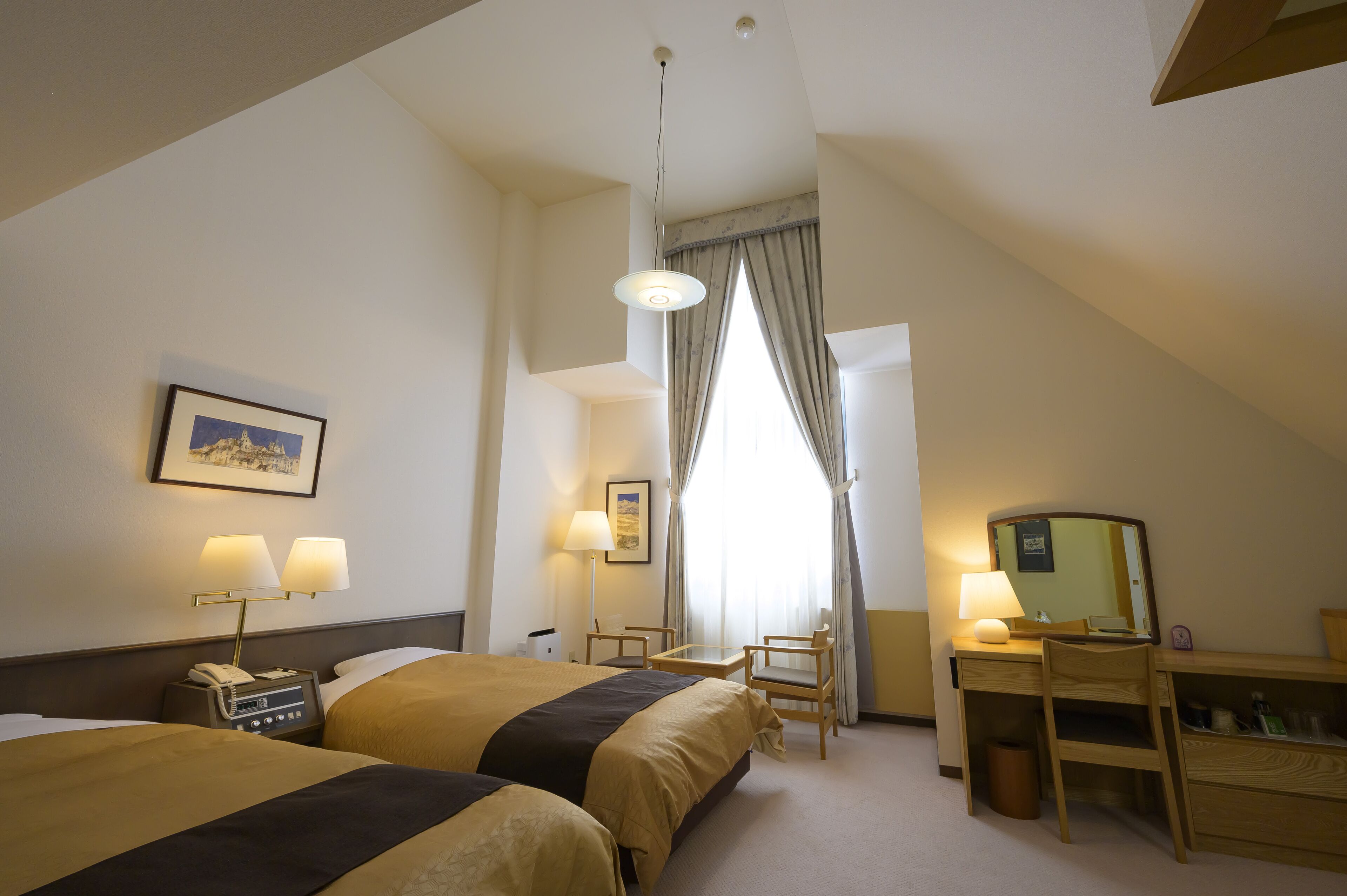 Hotelkamer met twee bedden, een bureau, een stoel, een lamp, een telefoon en een raam met gordijnen.