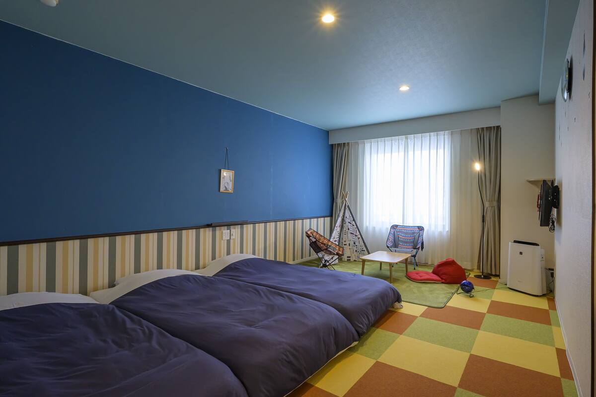 Hotellihuone, jossa on suuri sänky, pieni pöytä, tuoli ja värikäs, ruutukuviollinen lattia.