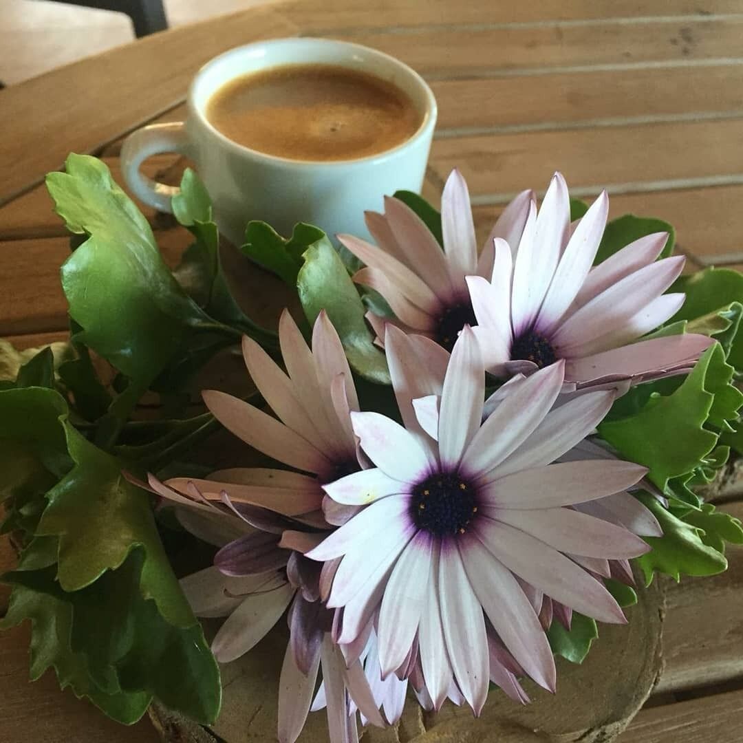 Uma chávena de café sobre uma mesa de madeira com um arranjo floral.