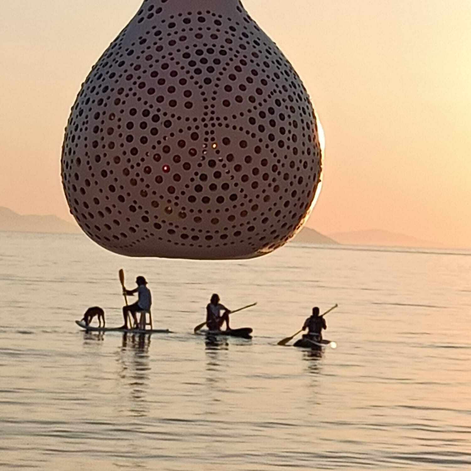 A large, textured spherical object above a calm body of water with people paddling in small boats.