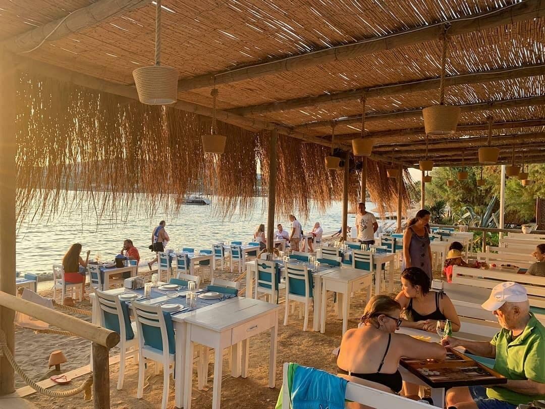Un espace extérieur aménagé pour les repas, avec des tables et des chaises, donnant sur un plan d’eau.
