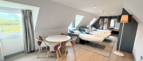 A modern interior with a round table, two sofas, a bed, and a view of a green landscape.