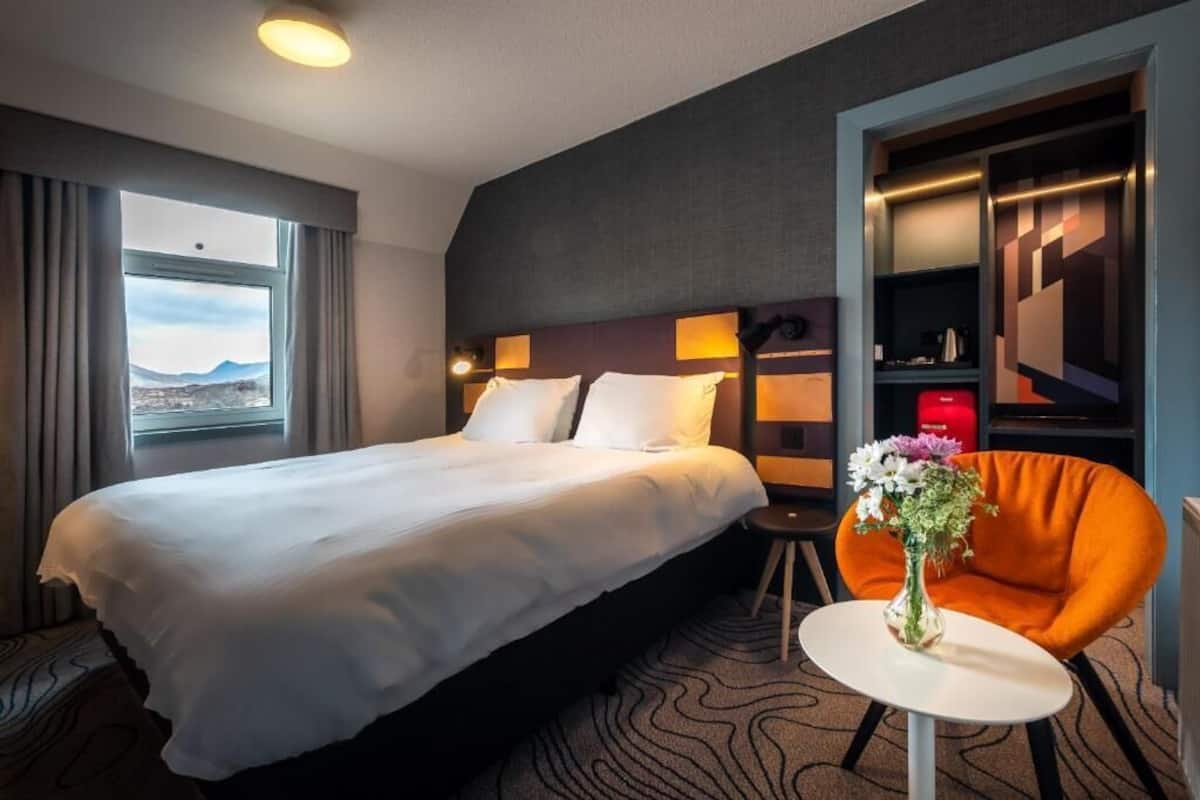 A hotel room with a large bed, a small round table with a vase of flowers, and a chair.
