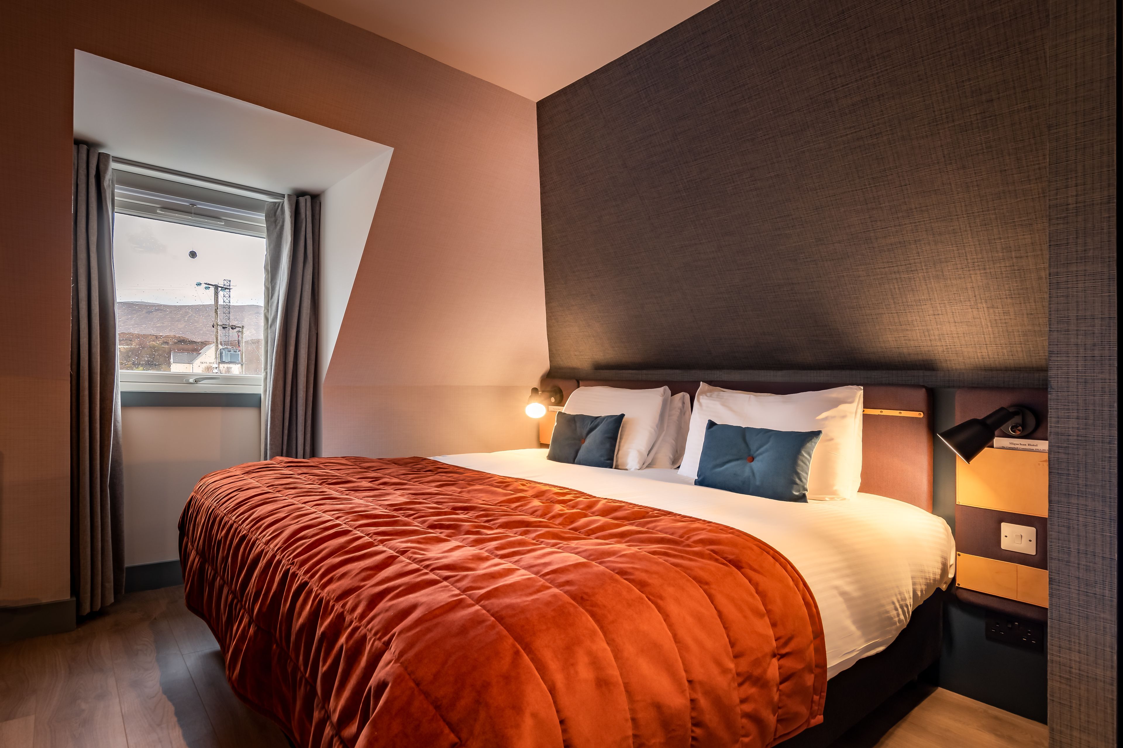 Een moderne hotelkamer met een groot bed, uitzicht naar buiten en een nachtkastje met een lamp.