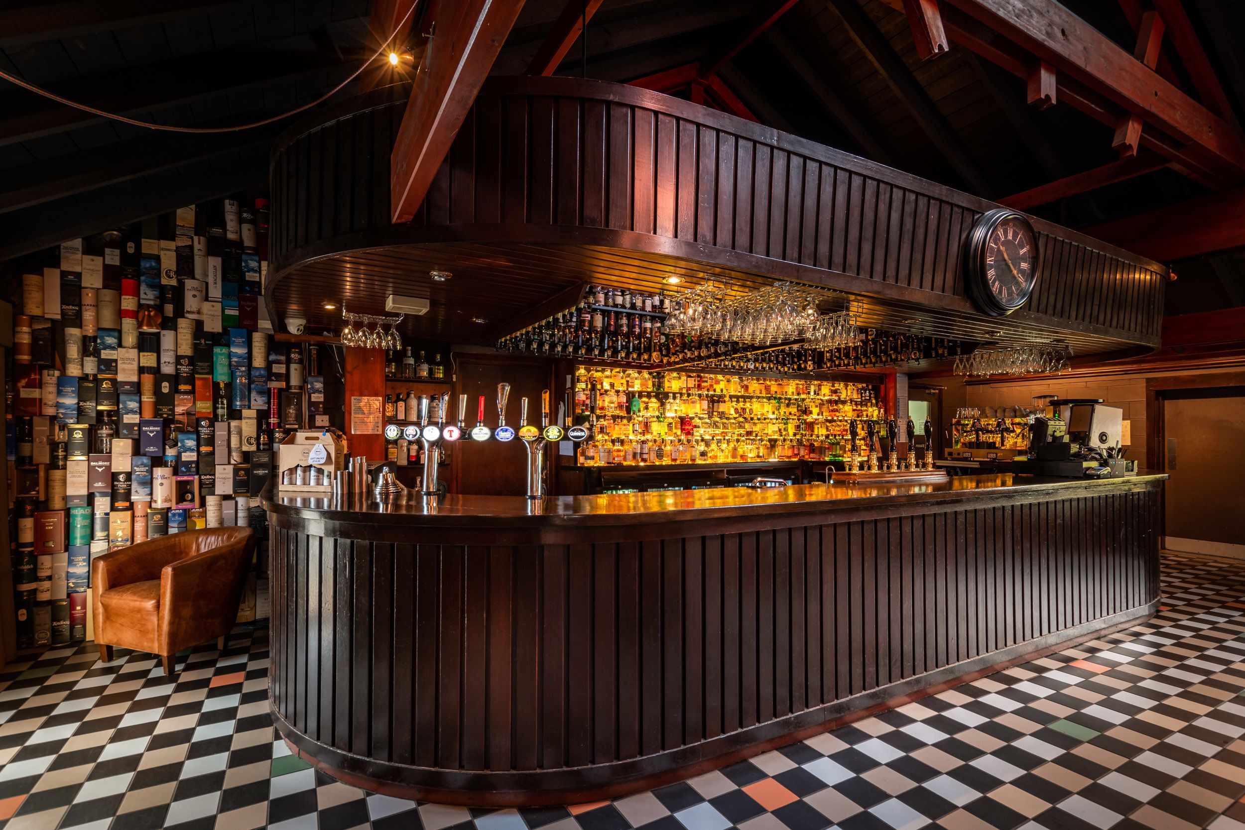 A bar with a checkered floor, wooden bar counter, and a wall of liquor bottles.