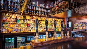 Un bar con scaffali pieni di bottiglie di liquori, un bancone e quattro rubinetti per la birra.