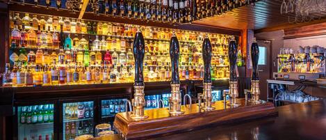 Una barra con varias estanterías llenas de botellas de licor, una barra y cuatro grifos de cerveza.