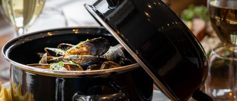 Una pentola nera con coperchio contenente cozze, accompagnata da un bicchiere di vino bianco e un bicchiere di vino rosso.