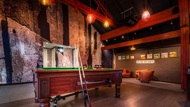A pool table with billiard balls and cues, wooden chairs, and framed artwork on the wall. - Sligachan Hotel (Minginish)