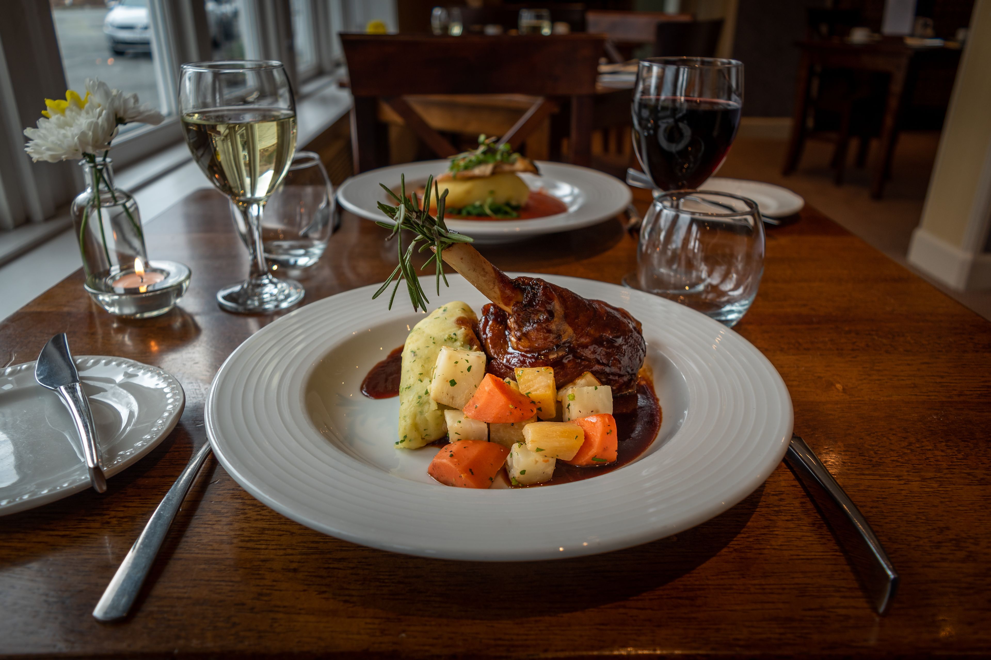 A dining table with a plate of food, a glass of white wine, and a candle.