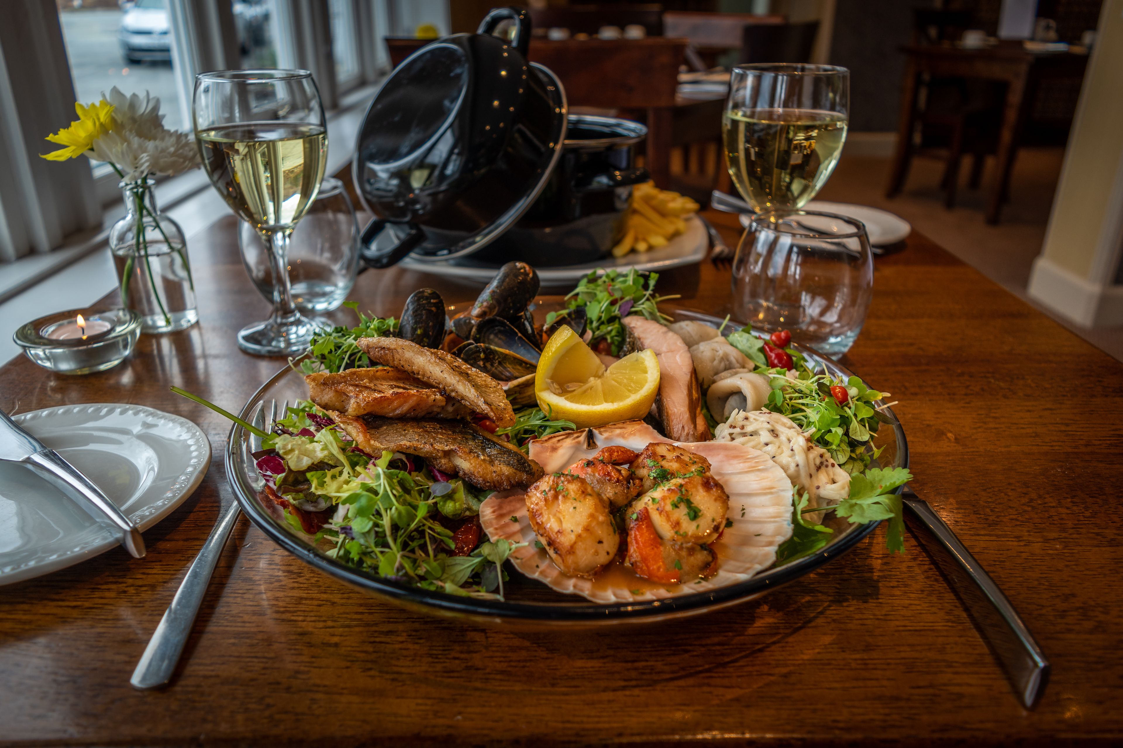 A dining table with a seafood platter, wine glasses, and a candle.