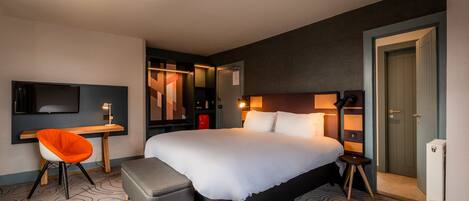 A modern hotel room with a large bed, a desk, a chair, and a TV.