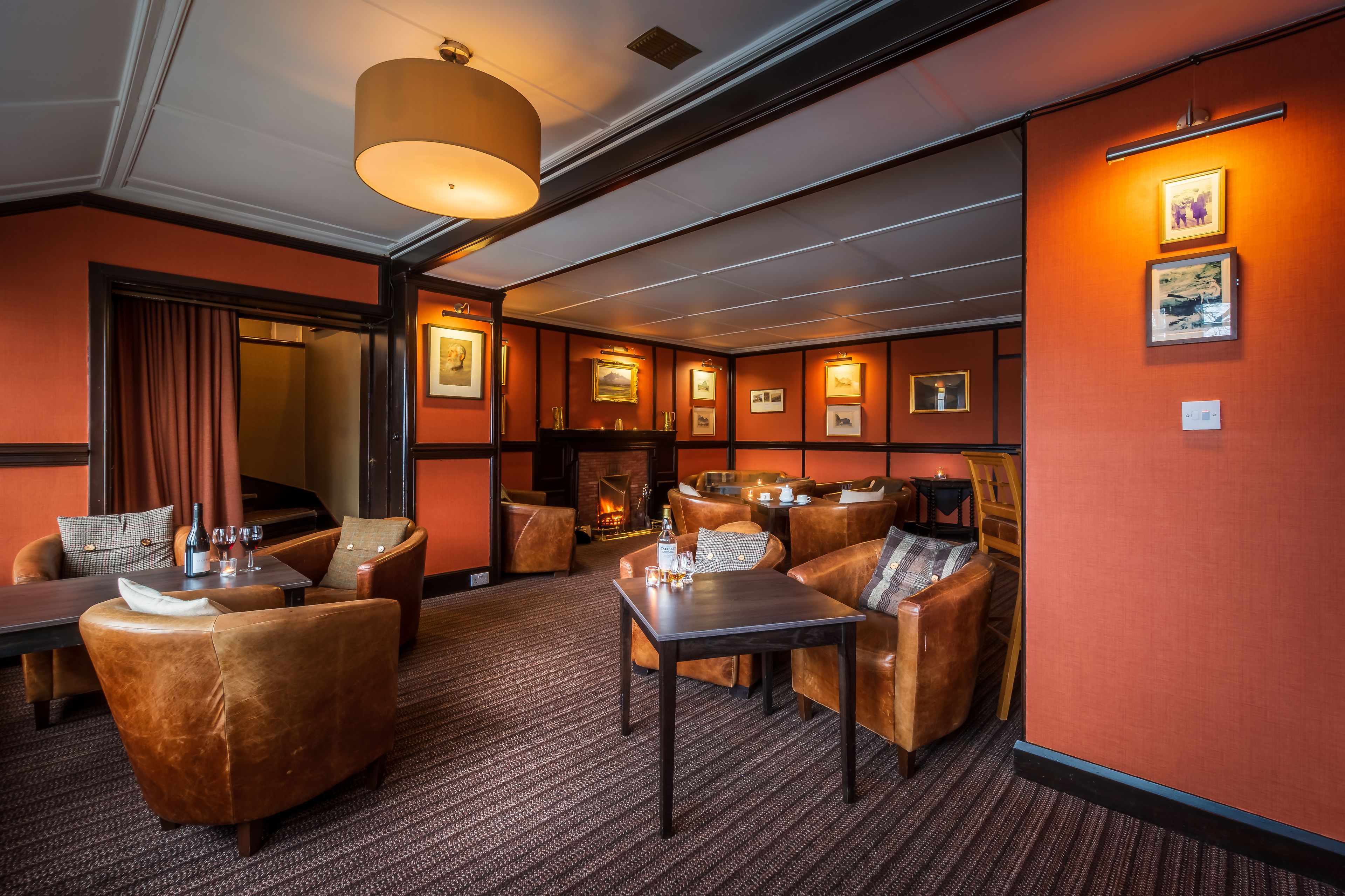A hotel lobby with leather seating, a fireplace, framed pictures on the walls, and a carpeted floor.