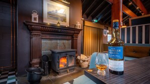 Una stanza accogliente con un camino, una bottiglia di whisky e un bicchiere su un tavolo di legno.