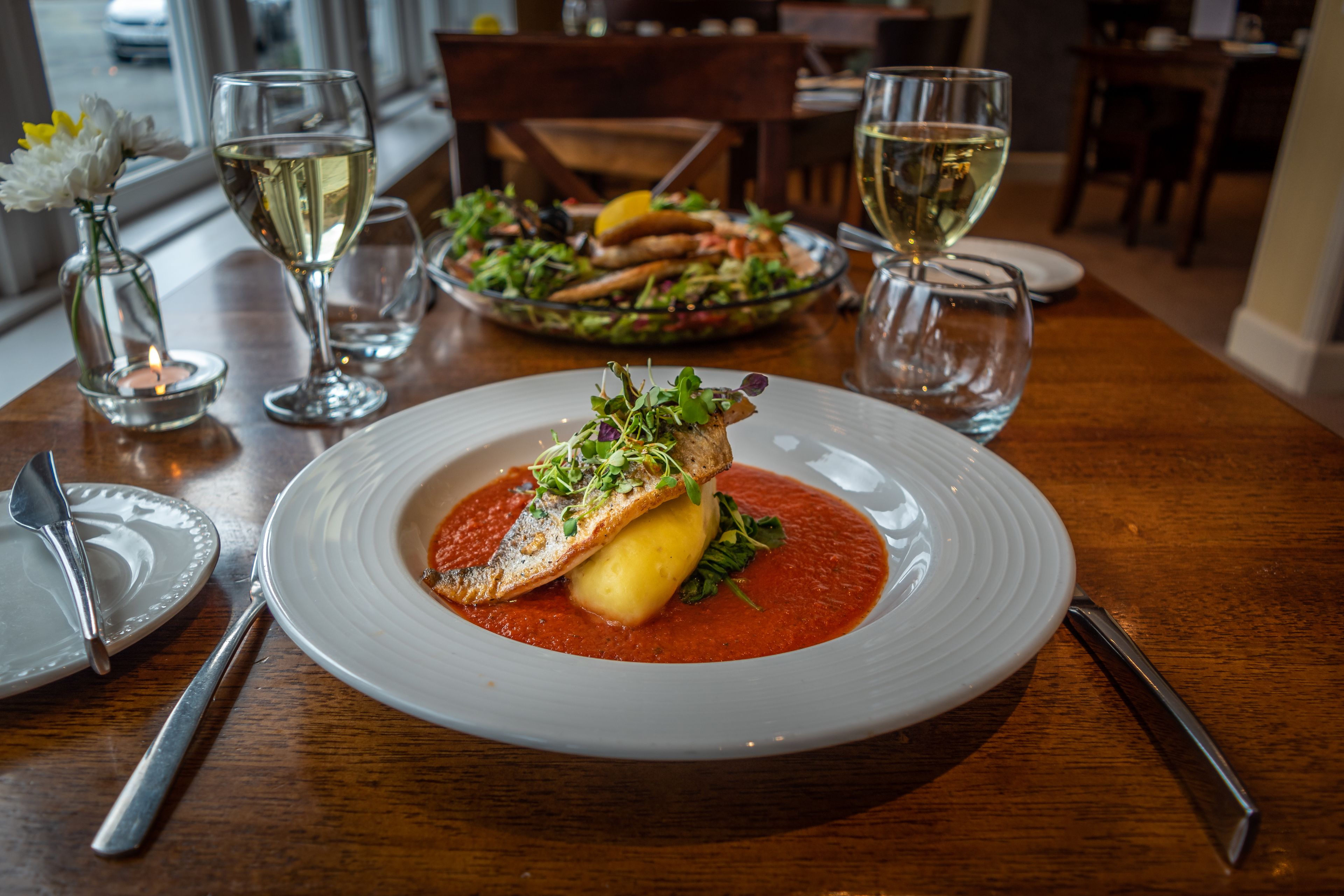 A dining table with a plate of food, a glass of white wine, and a candle.