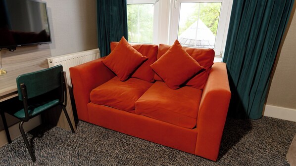 A room with a red sofa, a green chair, a flat-screen TV, and a window with curtains. - Sligachan Hotel (Minginish)