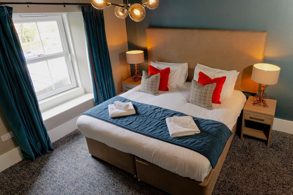 A hotel room with a large bed, two bedside tables with lamps, a window with curtains, and a view of the outside.
