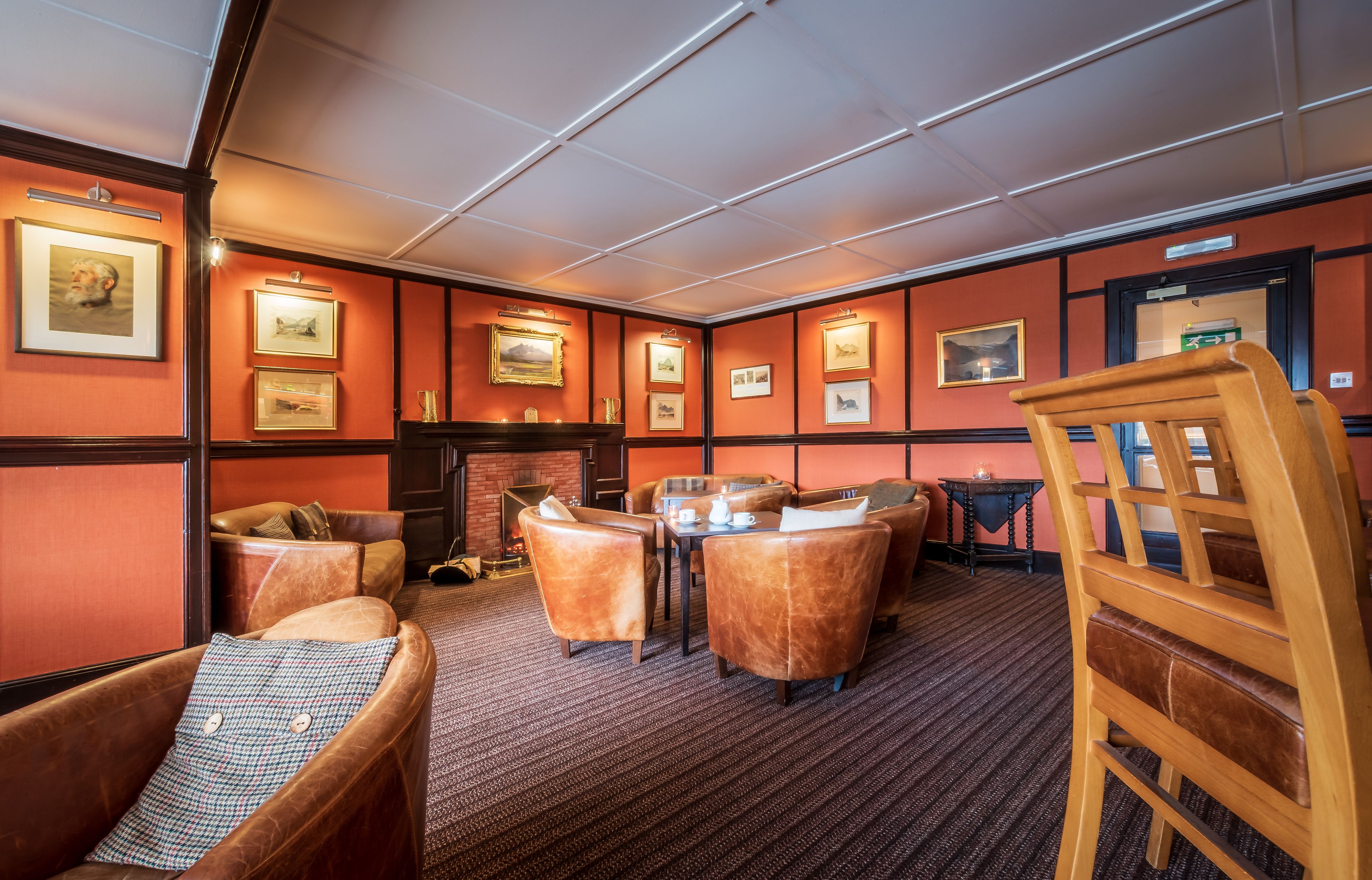 A room with leather armchairs, a fireplace, framed pictures on the walls, and a carpeted floor.