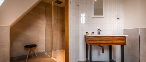 A modern bathroom with a glass shower, a wooden vanity, and a geometric tile backsplash.