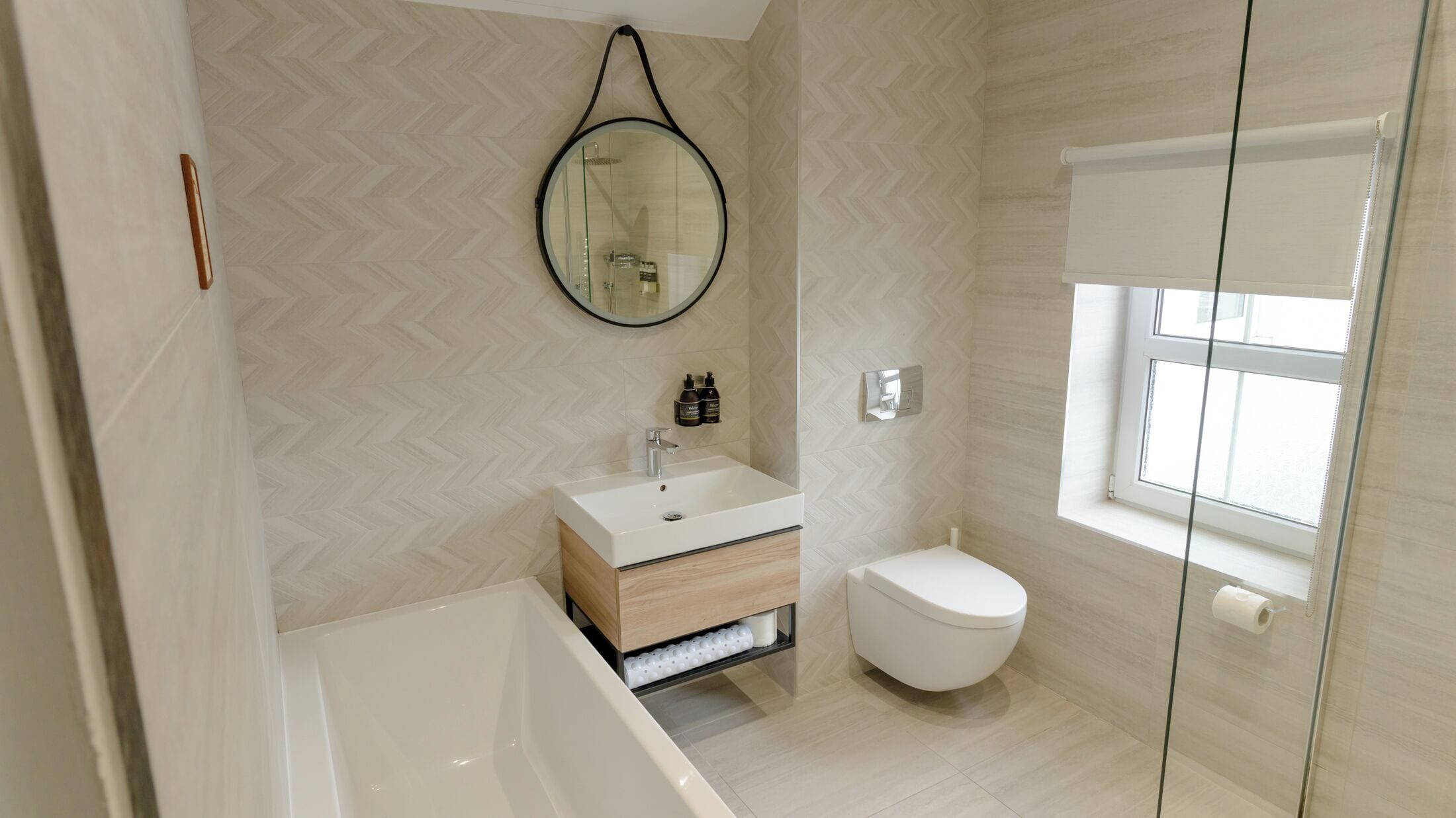 Un baño moderno con bañera, lavamanos e inodoro. Hay un espejo en la pared y una ventana que proporciona luz natural.