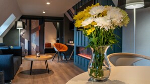 Un interno moderno con un vaso di vetro trasparente pieno di fiori su un tavolo, una parete blu e una zona salotto con divano e poltrone.