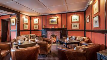 A cozy lounge area with leather sofas, a fireplace, and framed artwork on the walls.