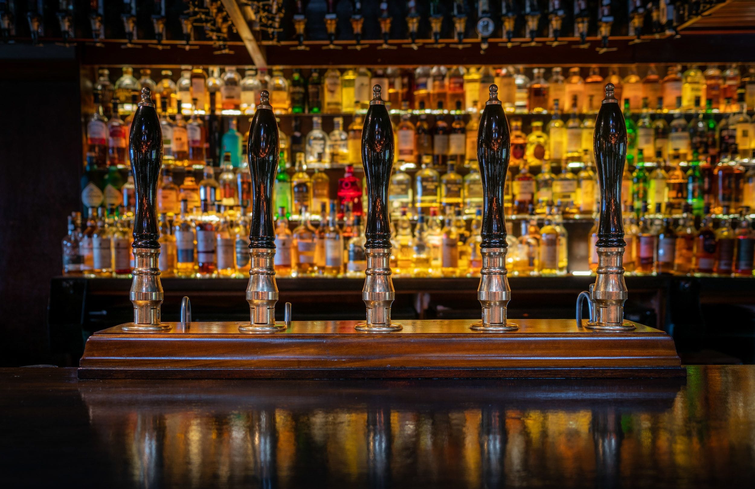 A bar with a row of taps and a background of various bottles.