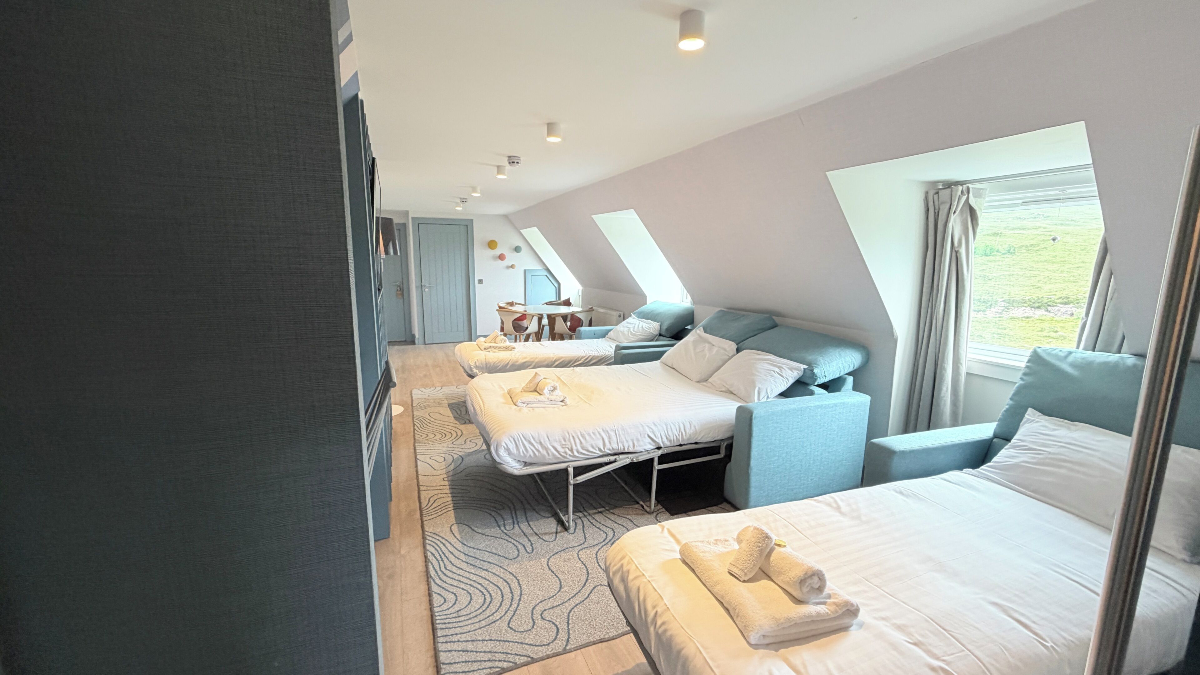 Une chambre d’hôtel moderne avec deux lits, un canapé, un bureau et une vue sur l’extérieur.