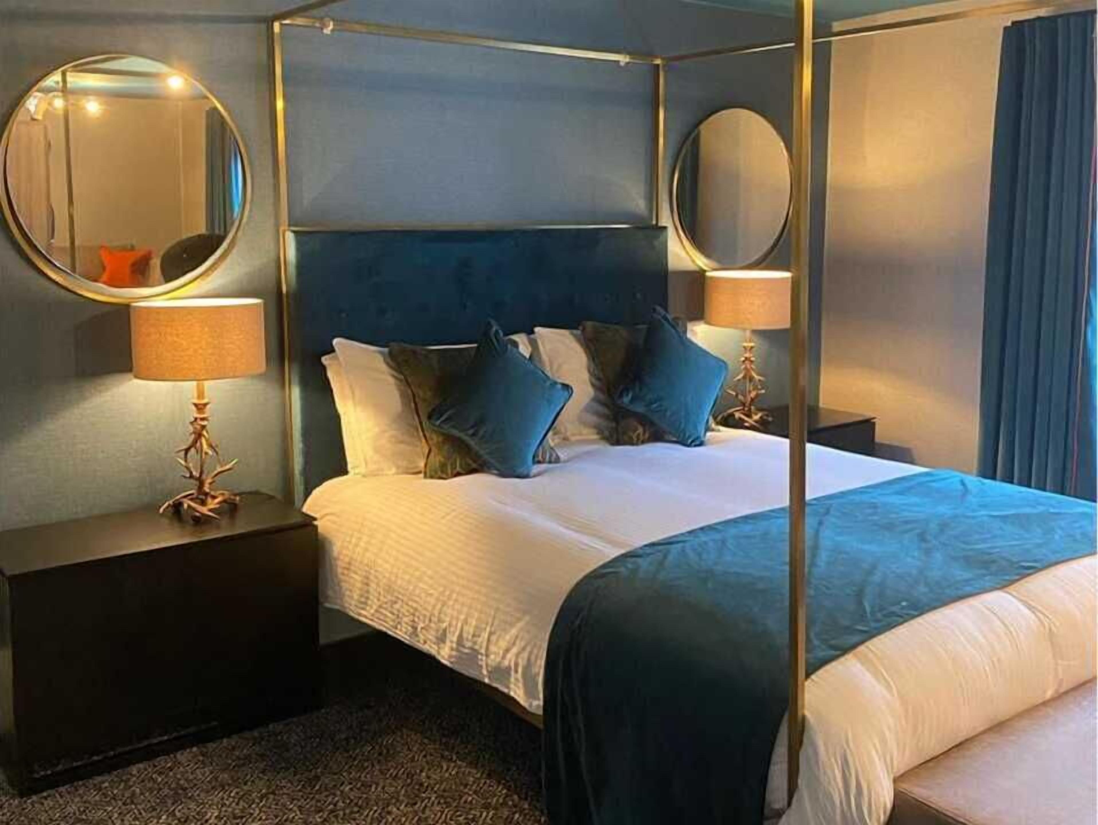 Uma cama de dossel com dossel, duas mesas de cabeceira e dois espelhos redondos.