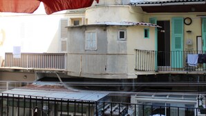 A balcony with a table and chairs, a red umbrella, and a building with multiple stories and balconies in the background. - Hotel Le Forum (Bastia)