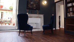 A room with a fireplace, two blue armchairs, a bookshelf, and a view of the outside. - Hotel Le Forum (Bastia)