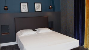 A hotel room with a large bed, two wall-mounted lamps, and two framed artworks above the bed. - Hotel Le Forum (Bastia)