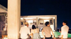 A group of people sitting outside a building with a modern architectural design, featuring large pillars and a spacious interior visible through the open structure. - Tamasa Service Apartment And Hotel (Phnom Penh)