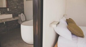 A modern bathroom with a white toilet, a sink, and a bathtub. There is a white bedside table with a pillow and a book. - Tamasa Service Apartment And Hotel (Phnom Penh)