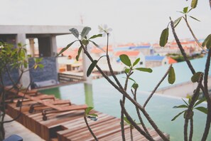 A wooden deck with lounge chairs overlooking a pool and a view of buildings in the background. - Tamasa Service Apartment And Hotel (Phnom Penh)