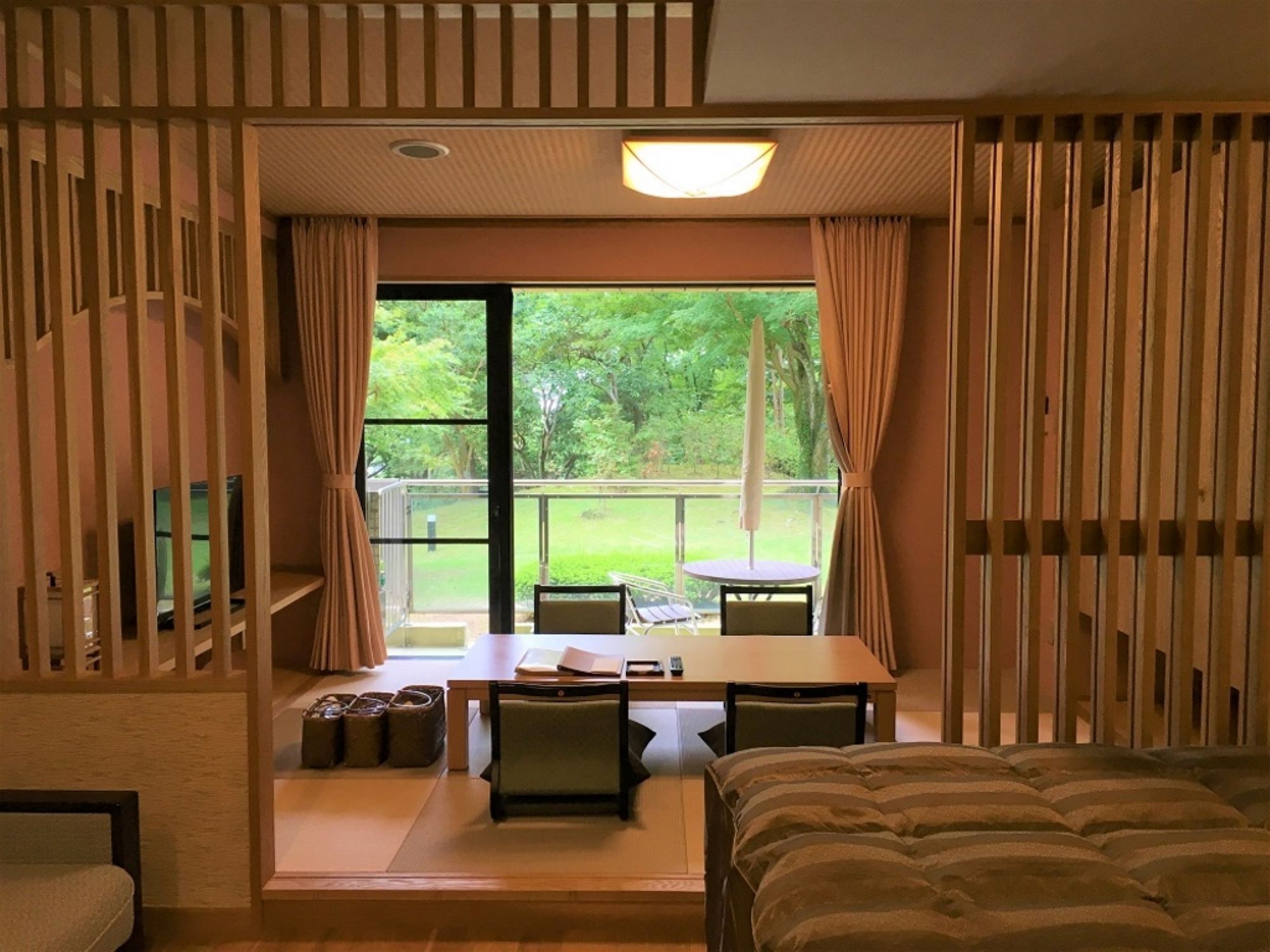 Quarto com cama, mesa, cadeiras e vista para o verde lá fora.