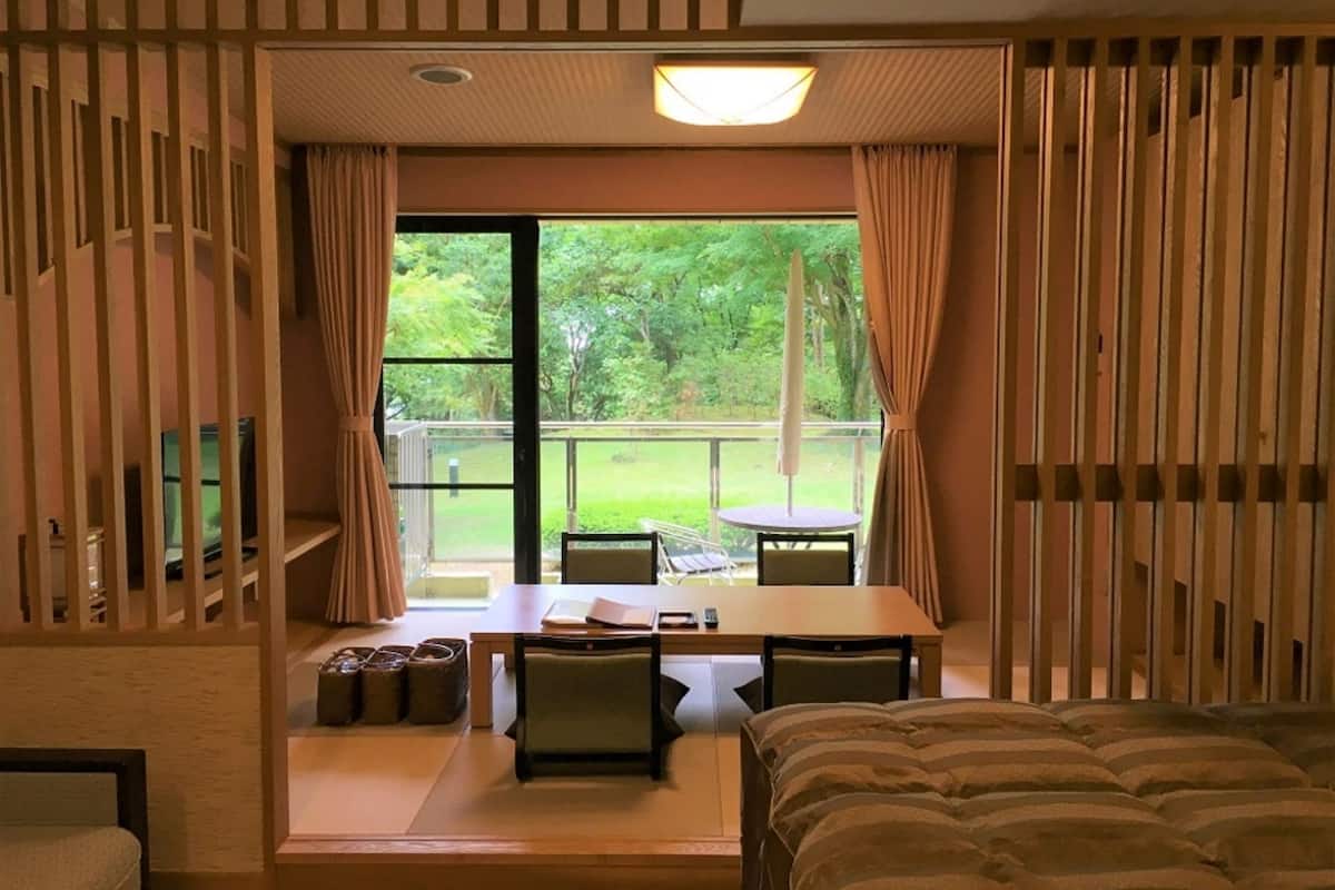 A room with a bed, a table, chairs, and a view of greenery outside.