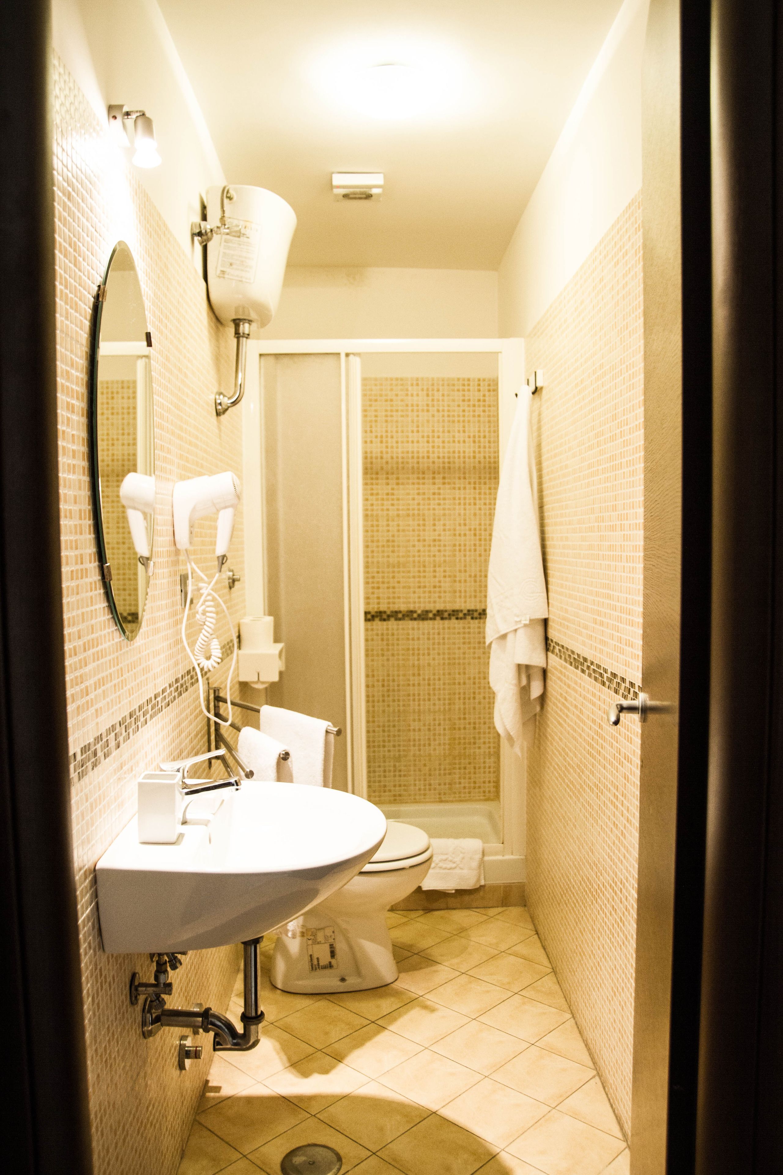A compact bathroom with a sink, mirror, hairdryer, and toilet.