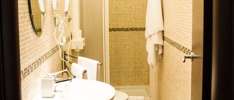 A compact bathroom with a sink, mirror, hairdryer, and toilet.