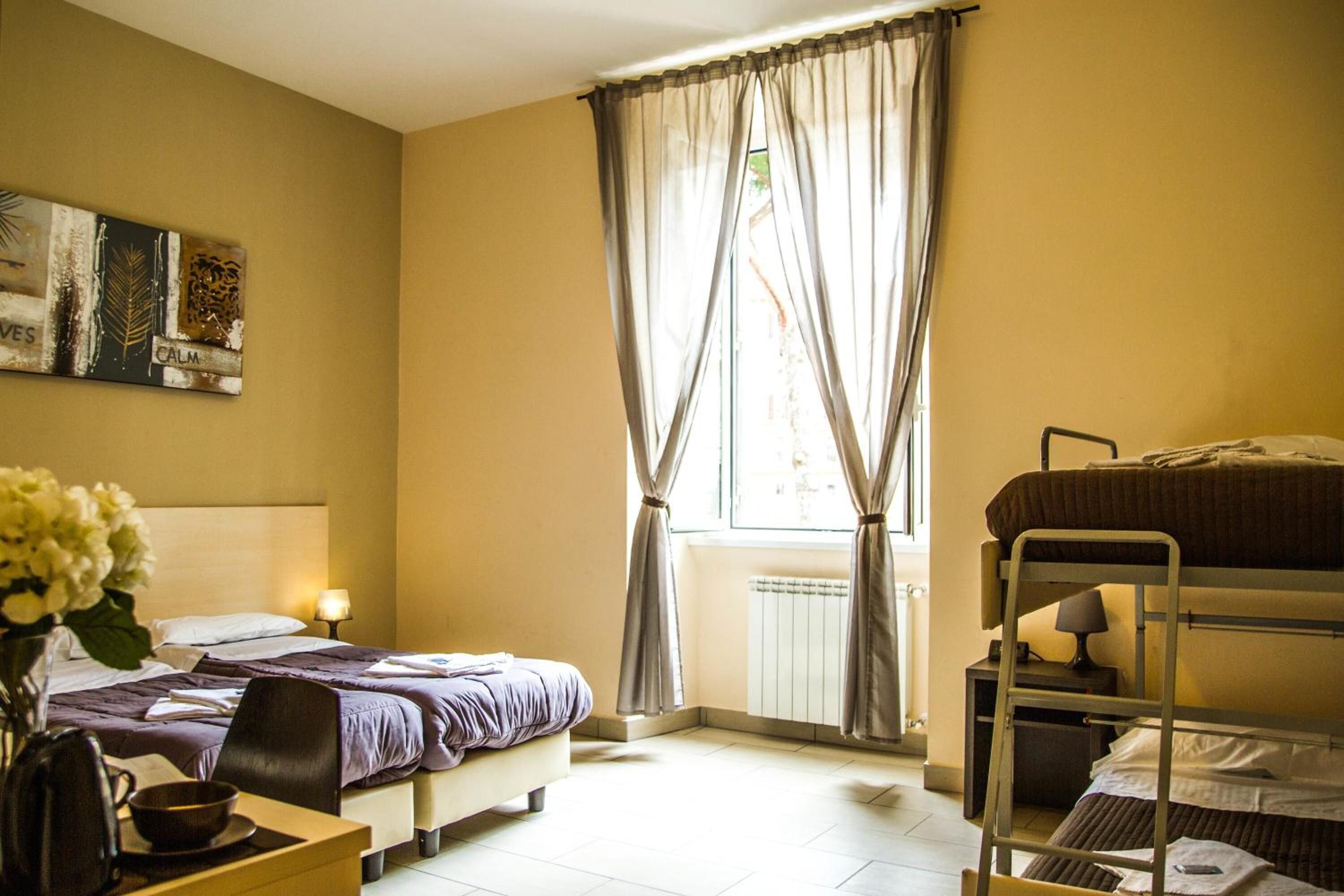 Une chambre d’hôtel avec un lit superposé, un lit simple, une table de chevet avec une lampe, une chaise et un tableau au mur.