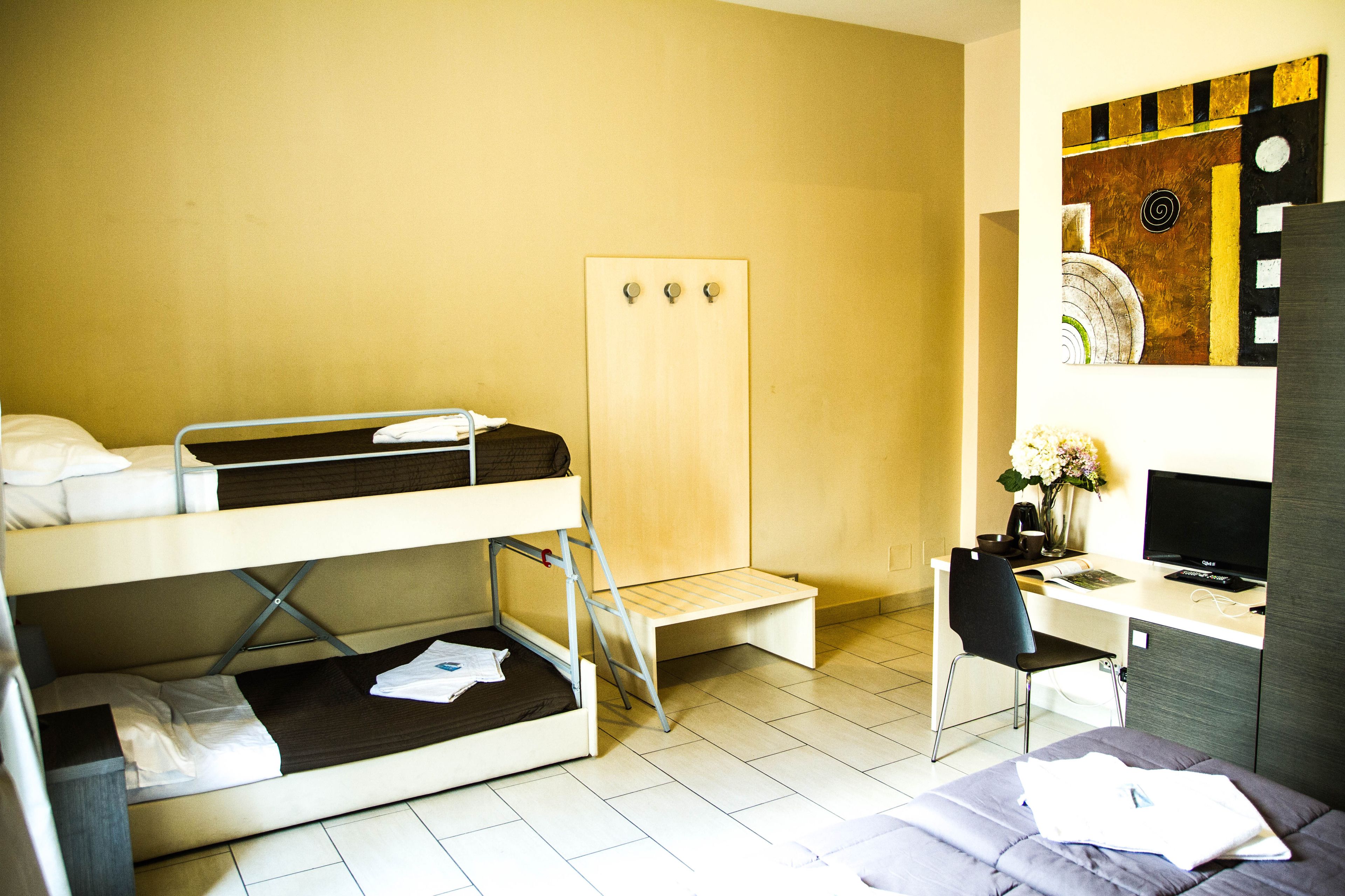 A dormitory-style room with bunk beds, a desk, a chair, a television, and a mirror.