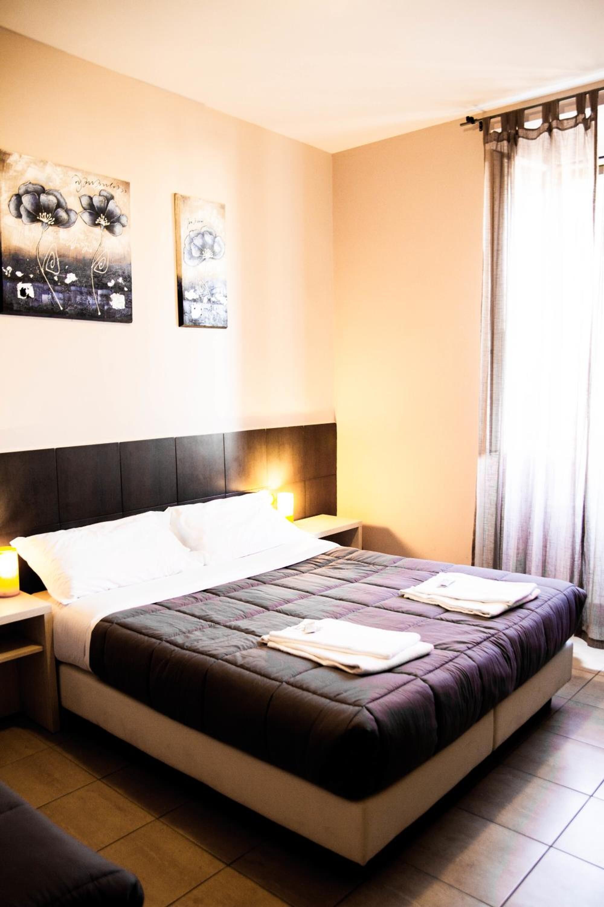 Une chambre d’hôtel avec un grand lit, deux tables de chevet, une tête de lit et une fenêtre avec des rideaux.